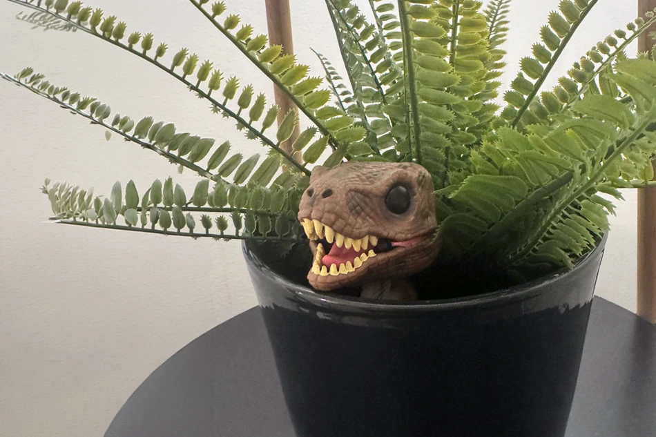 A toy dinosaur peeking out from a potted fern