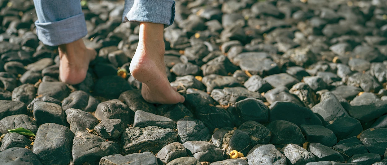 Bare feet stepping across dark stones on a sunlit path